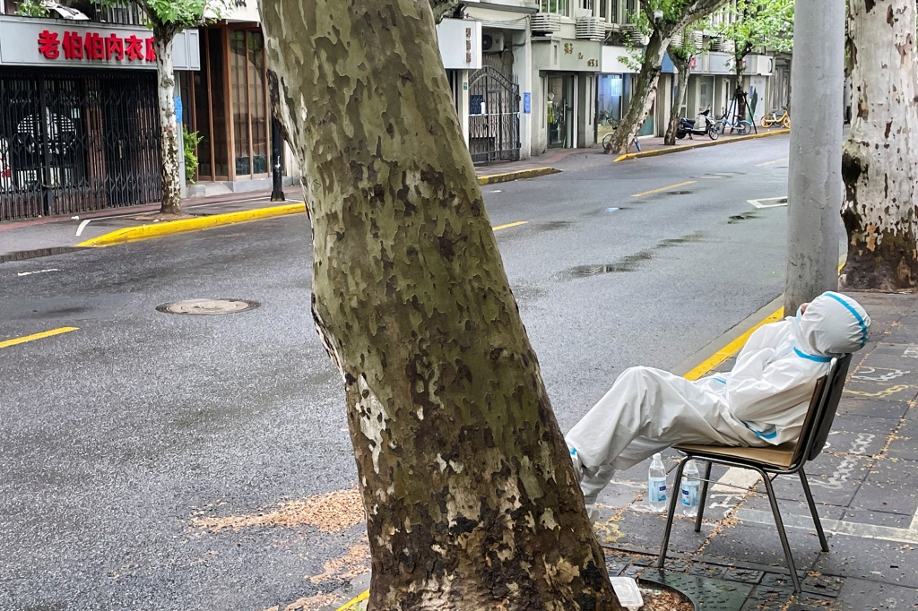 A tired medical worker sits along an empty street in Shanghai, China.