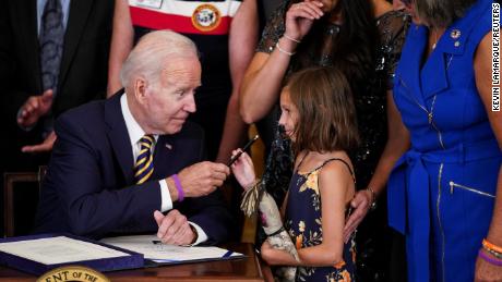 US President Joe Biden hands the pen of Brill Robinson, daughter of Sgt.  First Class Heath Robinson, as her mother, Danielle Robinson, poses by her side during a 'signing ceremony'  Sgt. First Class Heath Robinson delivers on our promises to address the Comprehensive Poisons Act (PACT) of 2022,