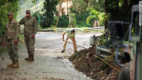 The National Guard directs traffic in Caye, Puerto Rico, where resident Luis Nogueira helps clear the road.