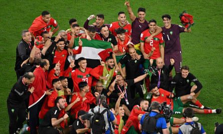 A group of players in their red shirts gather for a photo on the pitch, gesturing in celebration.  Several players raise the flag of Palestine in the middle of the group